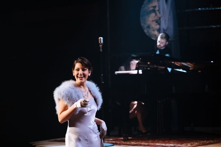 Two singers stand near a piano during a performance